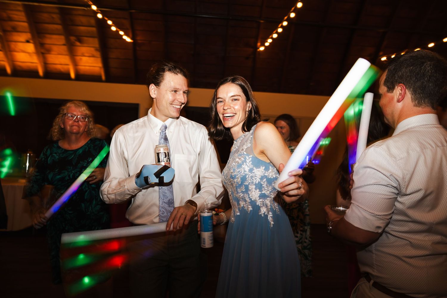 People dancing and celebrating at a lively wedding reception with colorful lights and decorations.