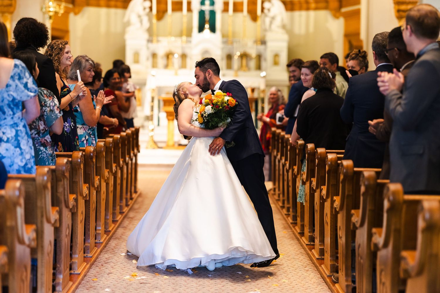 Wedding ceremony in an elegant church with wooden pews filled with guests watching a couple at the altar.