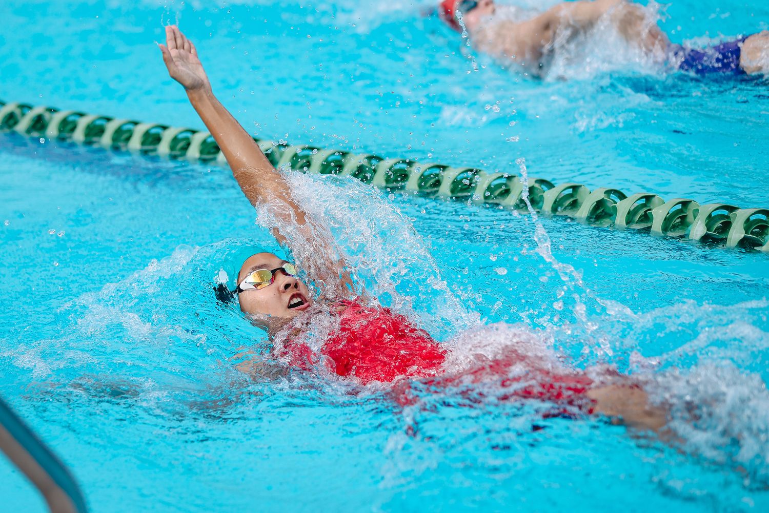 Swimmer executes backstroke technique during competitive race in pool.