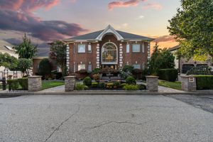 Grand estate entrance with stone pillars and circular driveway at sunset.