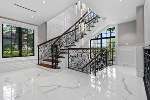 Contemporary white marble staircase with ornate black metal railings and recessed lighting.