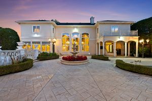 Panoramic exterior view of a luxurious white mansion with illuminated windows at dusk.