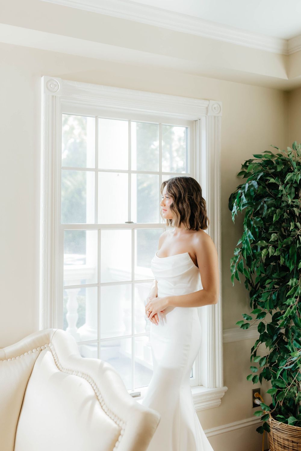 Elegant bridal portraits taken in a bright sunlit room with white decor and potted plants.