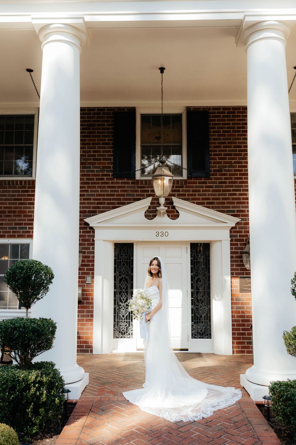 Bridal portraits captured under white columns at a classic brick building entrance.