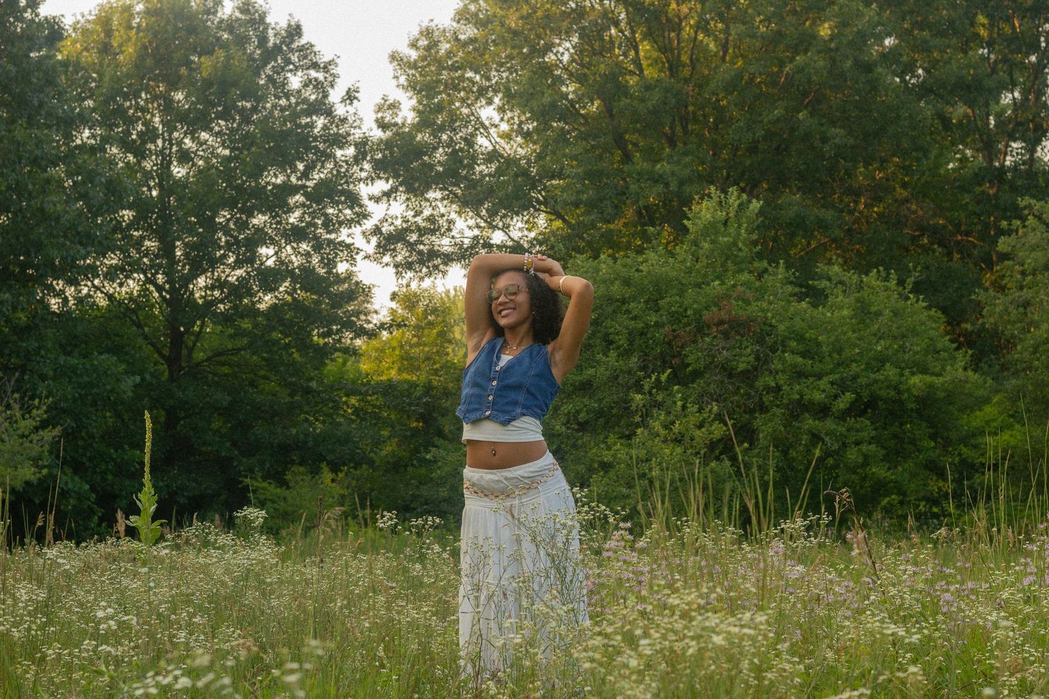 A girl poses in a denim vest and boho maxi skirt in a field of flowers for her senior photos.