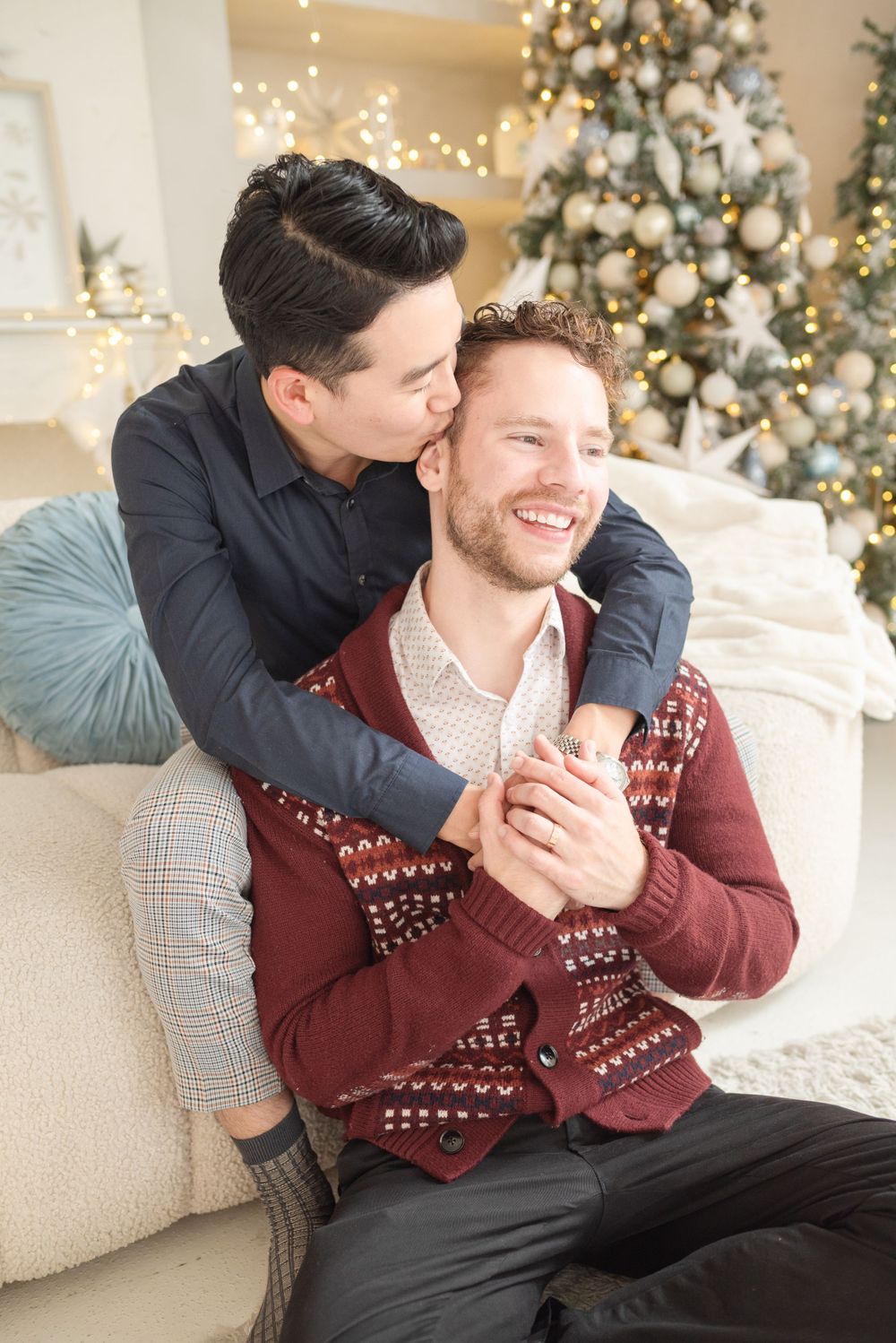Intimate holiday moment shared on cream couch with decorated Christmas tree backdrop.