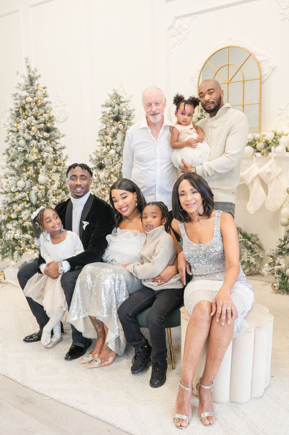 A multigenerational family in formal attire poses together for a holiday portrait with decorated trees.