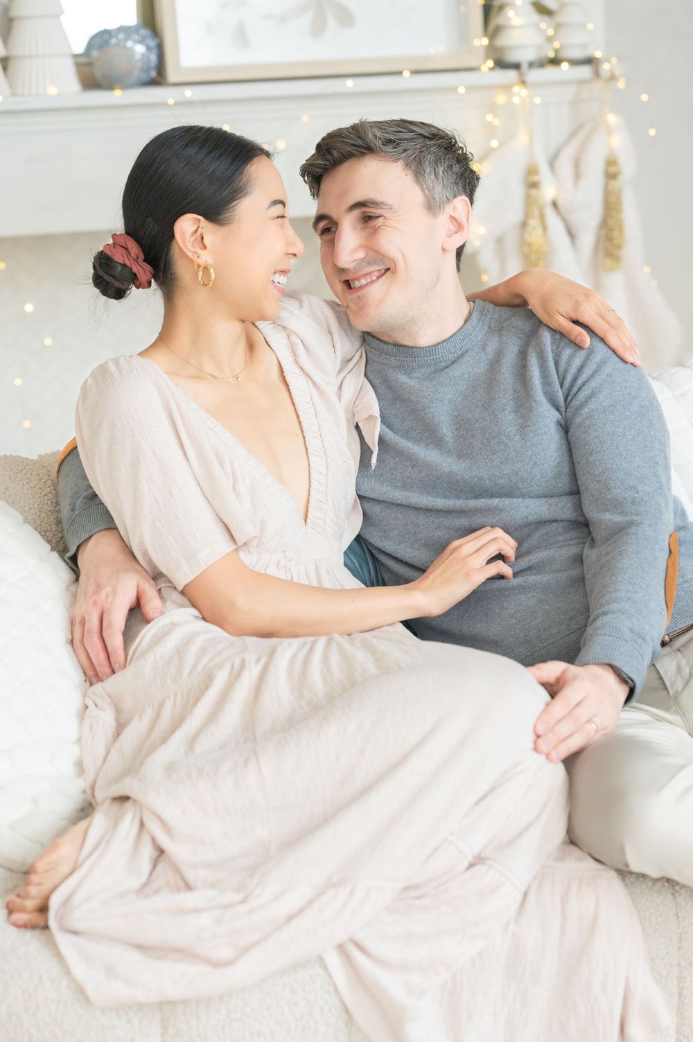 Romantic couple sharing an intimate moment on a white couch with magical holiday lights in the background.