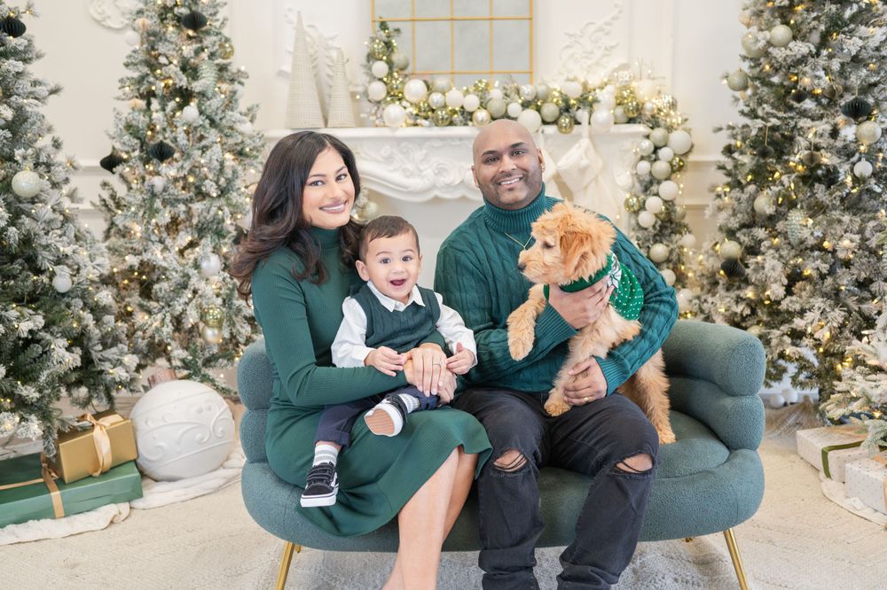 Cozy family holiday portrait with a teddy bear on blue armchair surrounded by Christmas trees.