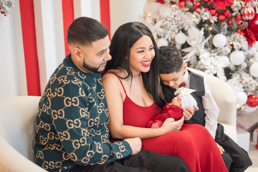 A family sharing a joyful moment in front of a Christmas tree with red and white decorations.