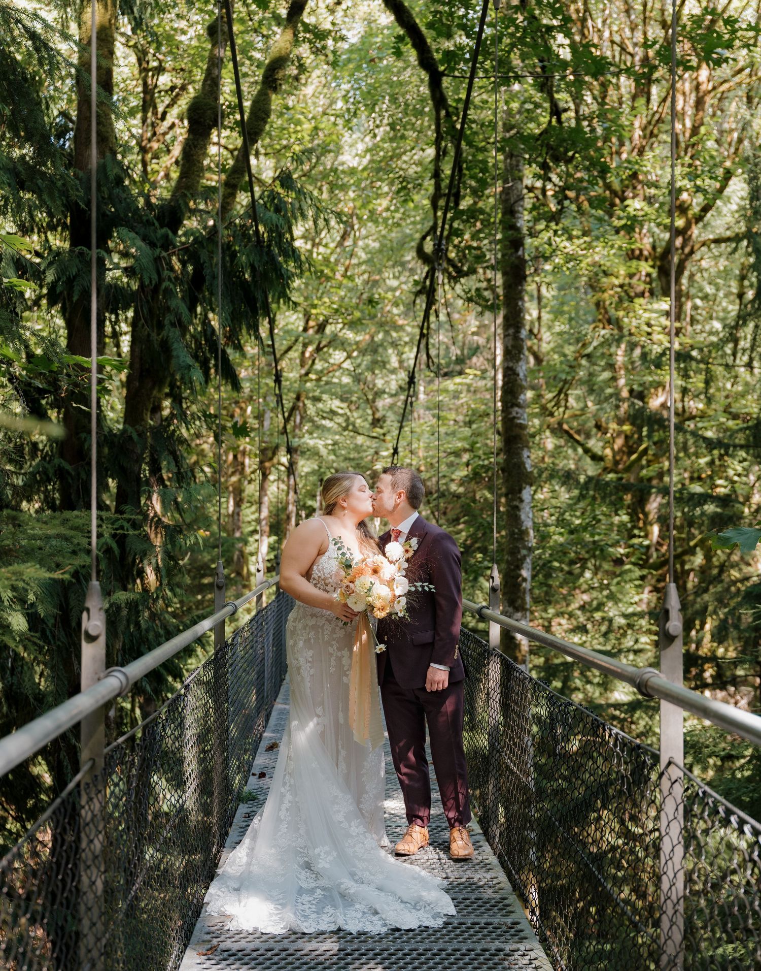 A couple sharing a romantic moment on a metal suspension bridge surrounded by lush green forest canopy.