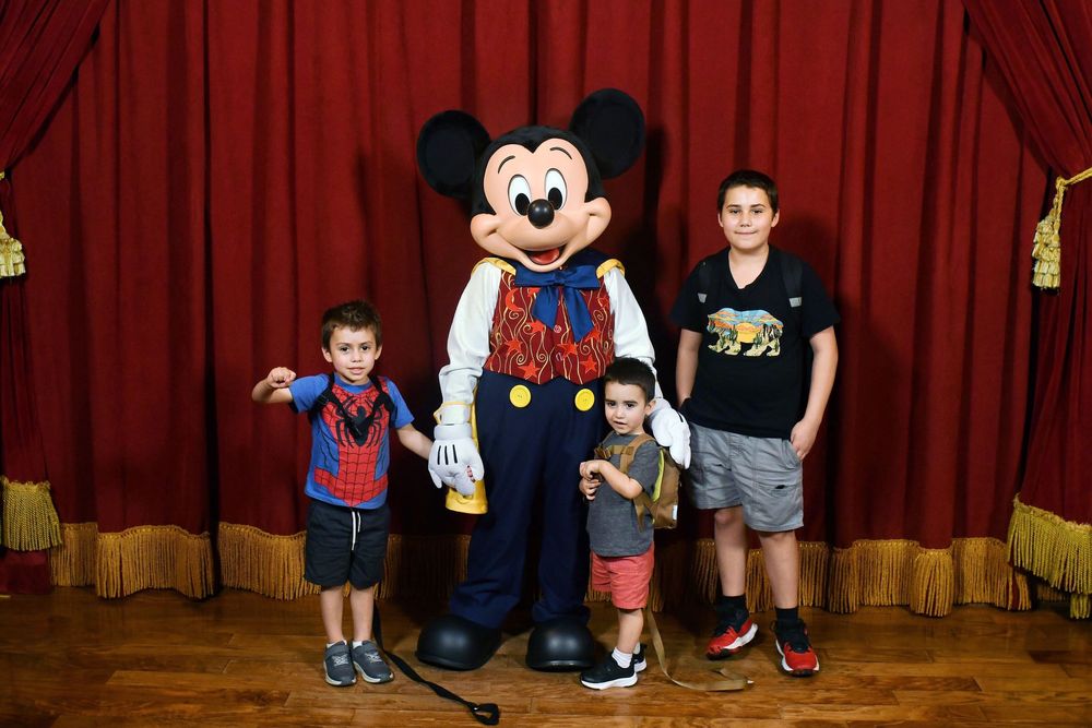 A group poses with Mickey Mouse character against a red curtain backdrop at a Disney meet and greet.