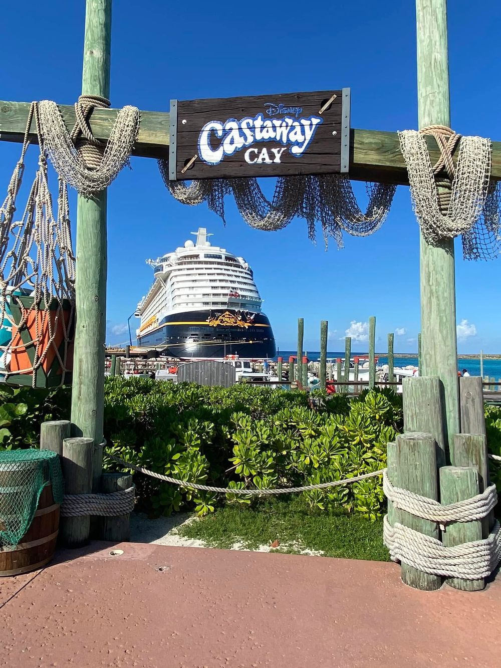 A Disney cruise ship docked at Castaway Cay with fishing nets and wooden posts decorating the entrance to the pier.