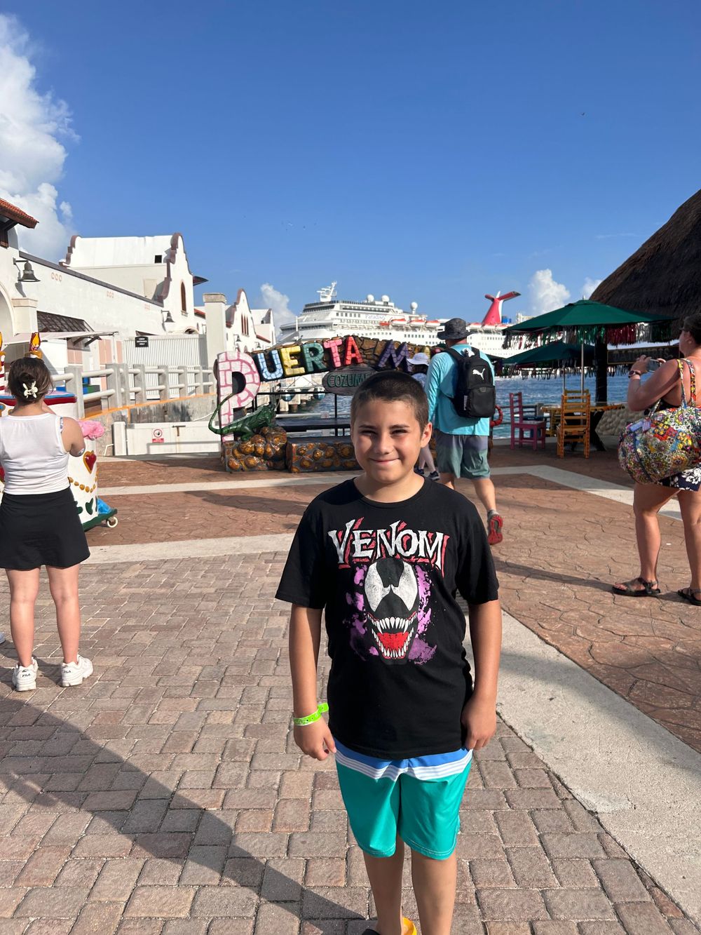 Someone wearing a Venom t-shirt and turquoise shorts stands in a tourist area with buildings in background.
