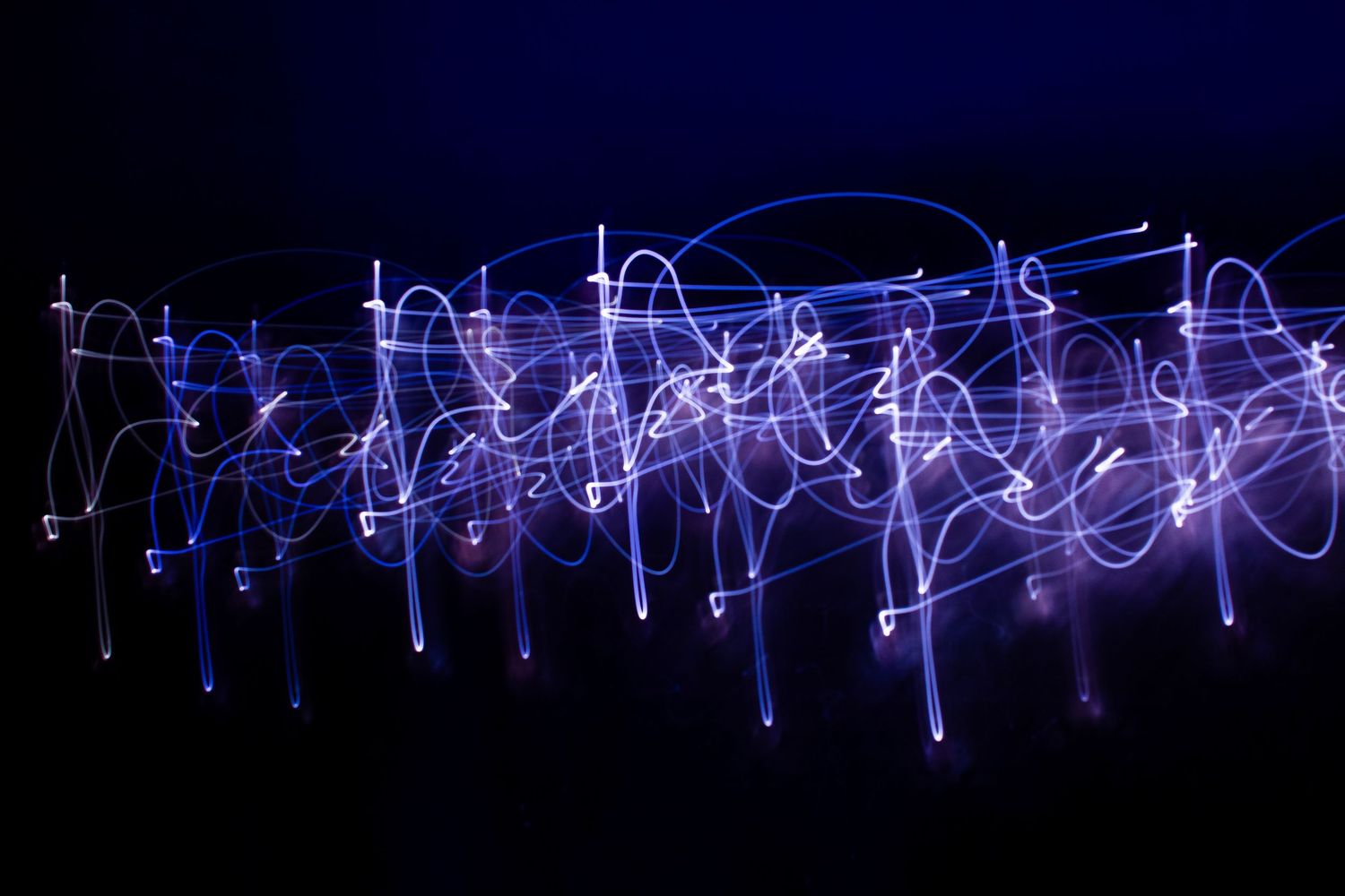 Abstract light painting photograph showing blue and white light trails swirling against a dark background.