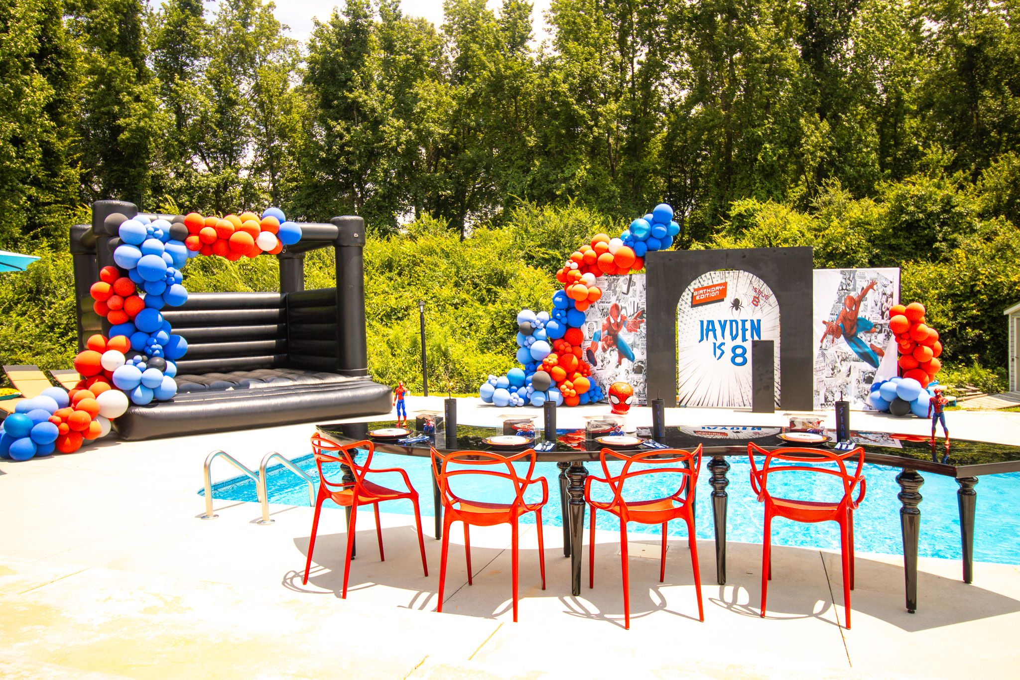 Outdoor party space decorated with red and blue balloons near a pool with red metal chairs.