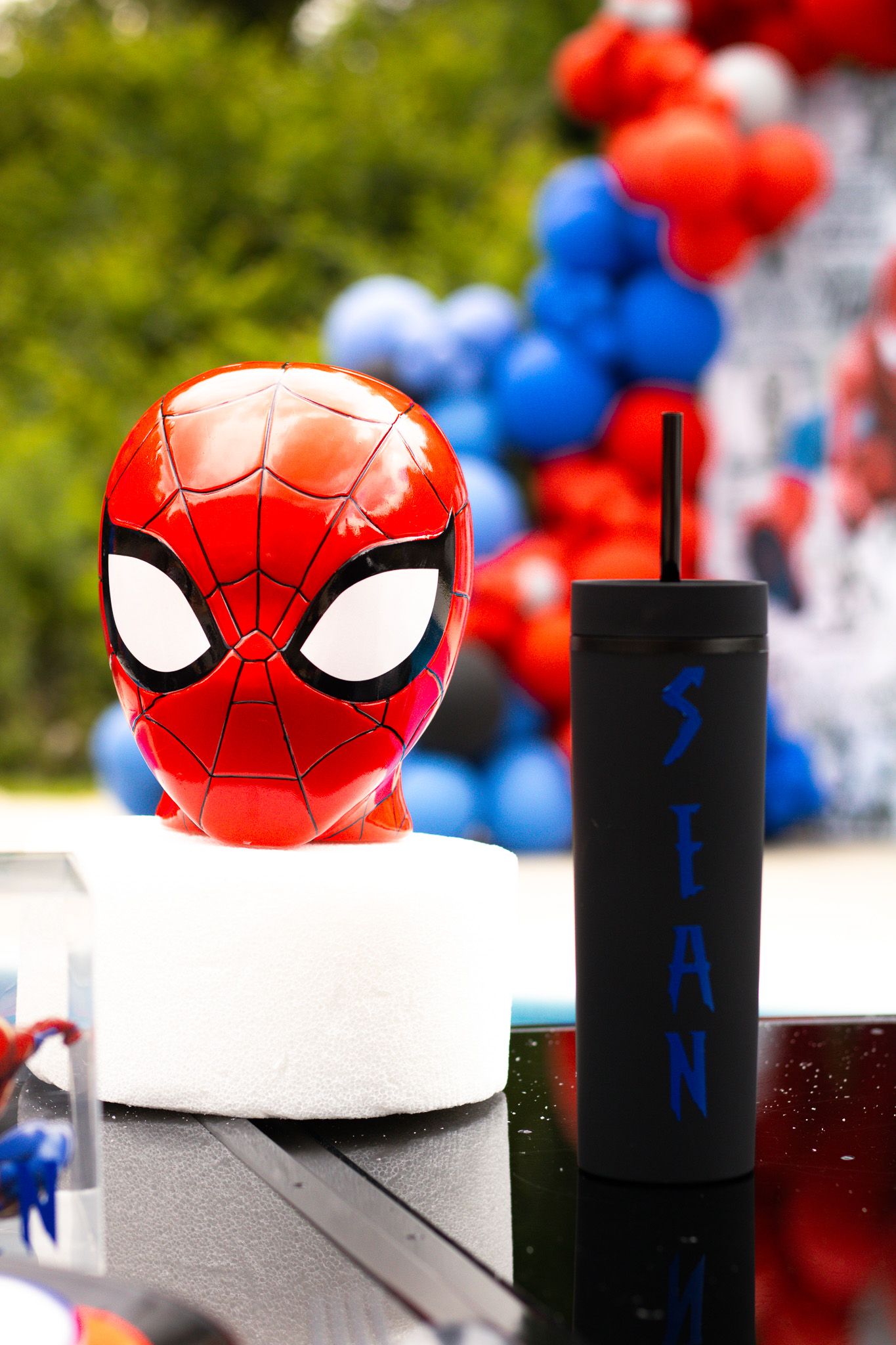 Spider-Man mask decoration and personalized black tumbler displayed with balloon decorations.