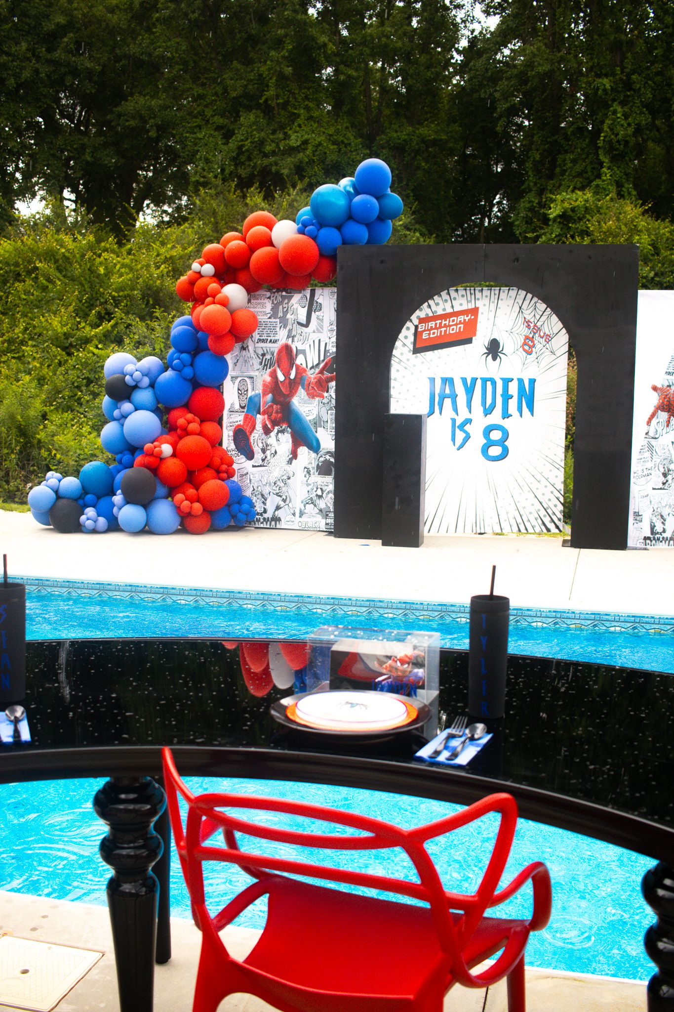 Birthday party setup with balloon arch and decorative backdrop near swimming pool.