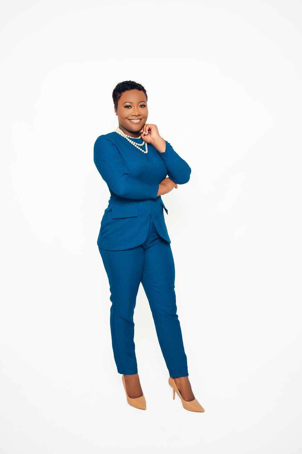 A person in a fitted royal blue business suit and nude heels poses confidently against a white background.
