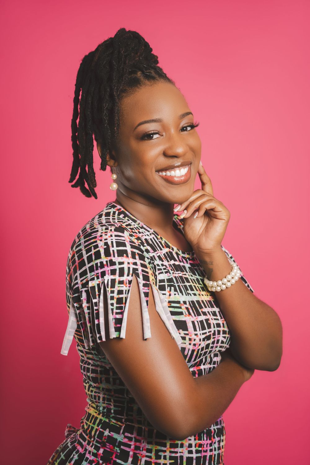Portrait of someone wearing a geometric patterned dress posing cheerfully against a pink background.