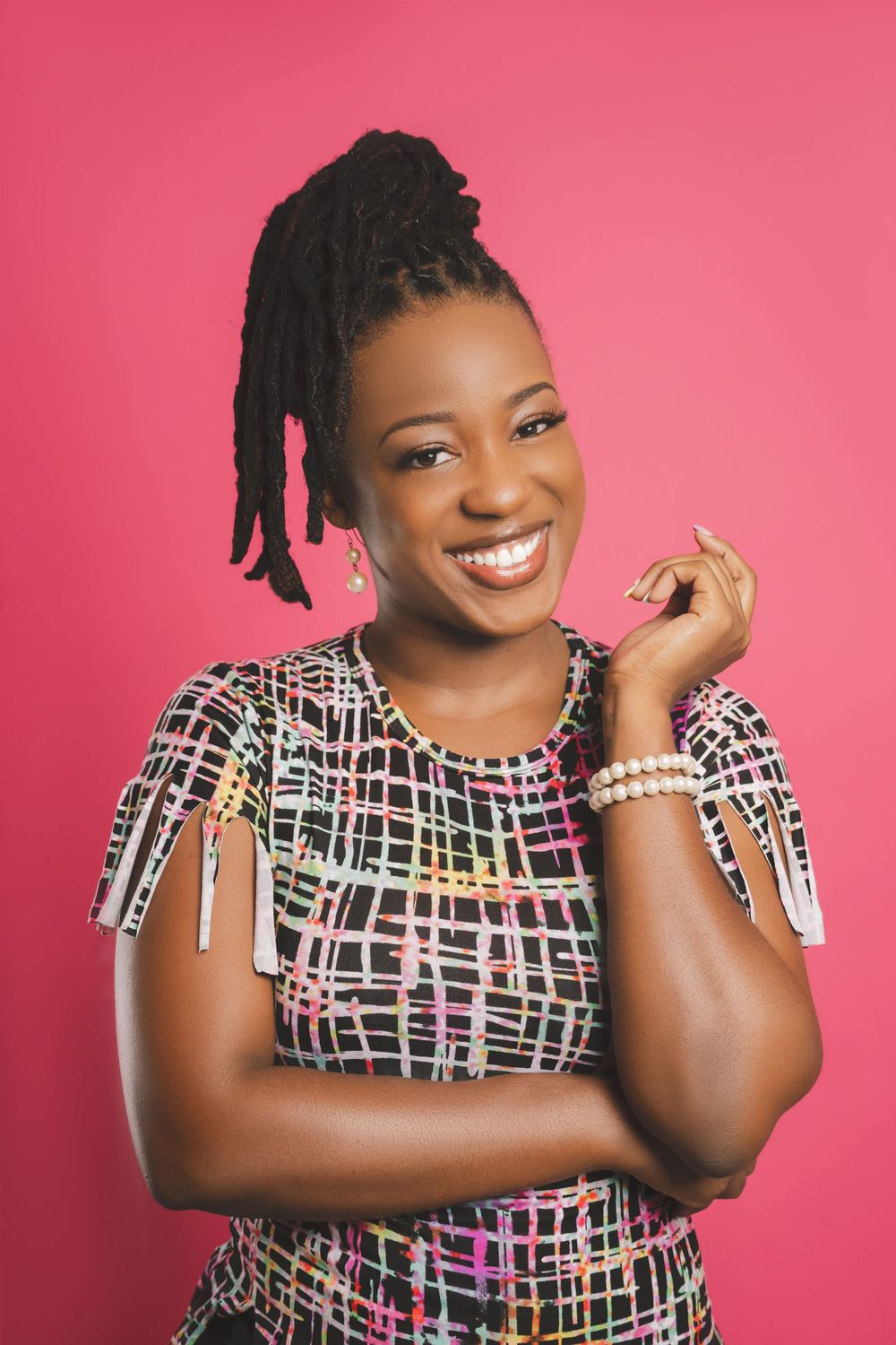 A smiling person wearing a patterned dress with geometric designs poses against a pink background.