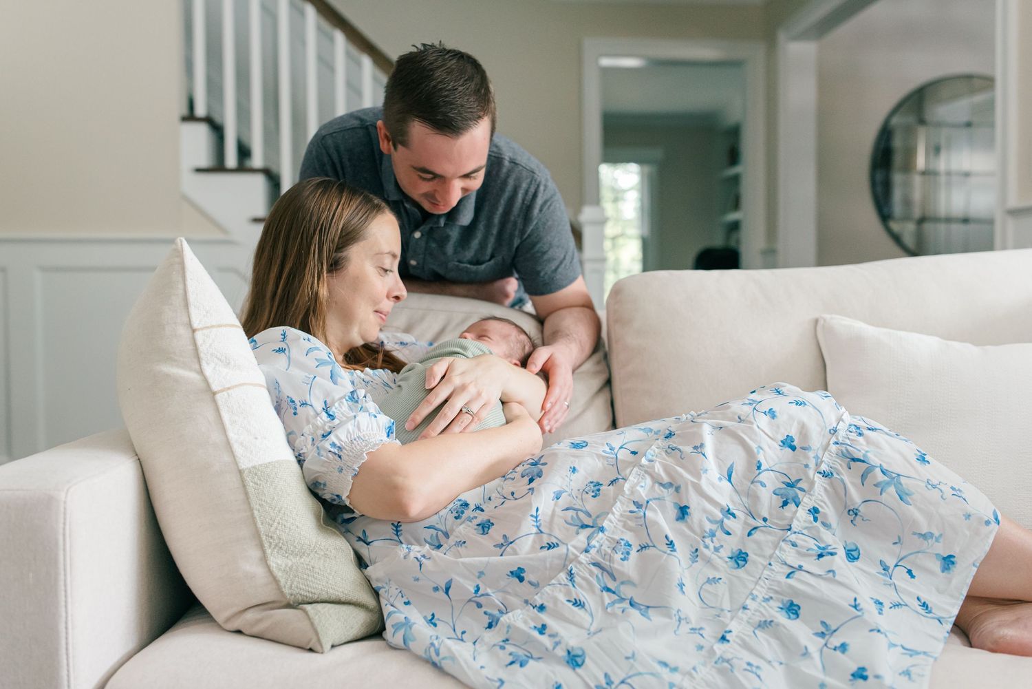 Mother holding newborn on the couch with father looking down at them during in-home lifestyle session in Fair Haven, NJ.