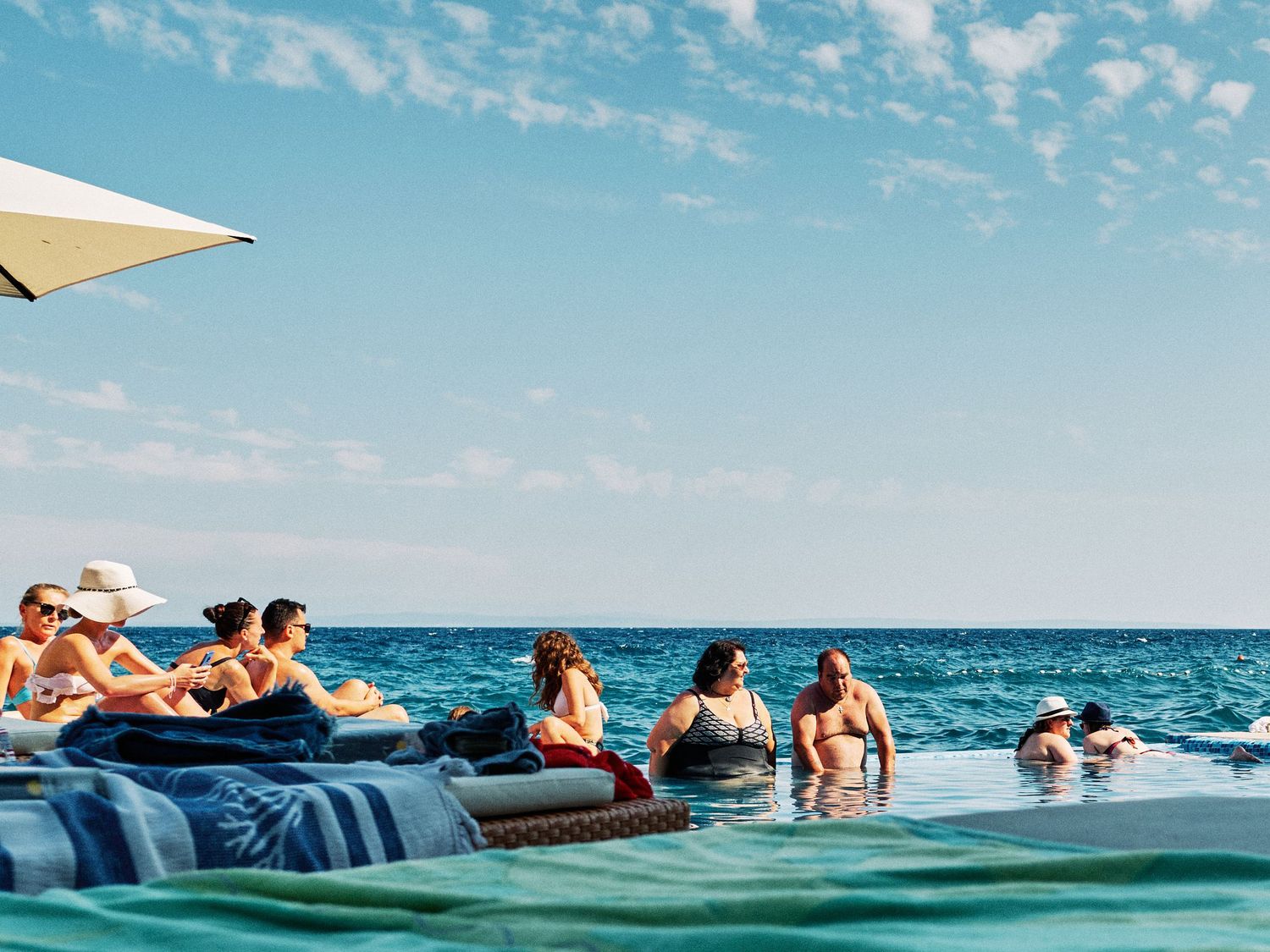 People enjoying a summer day lounging on floating rafts in blue ocean water under bright sunny skies.