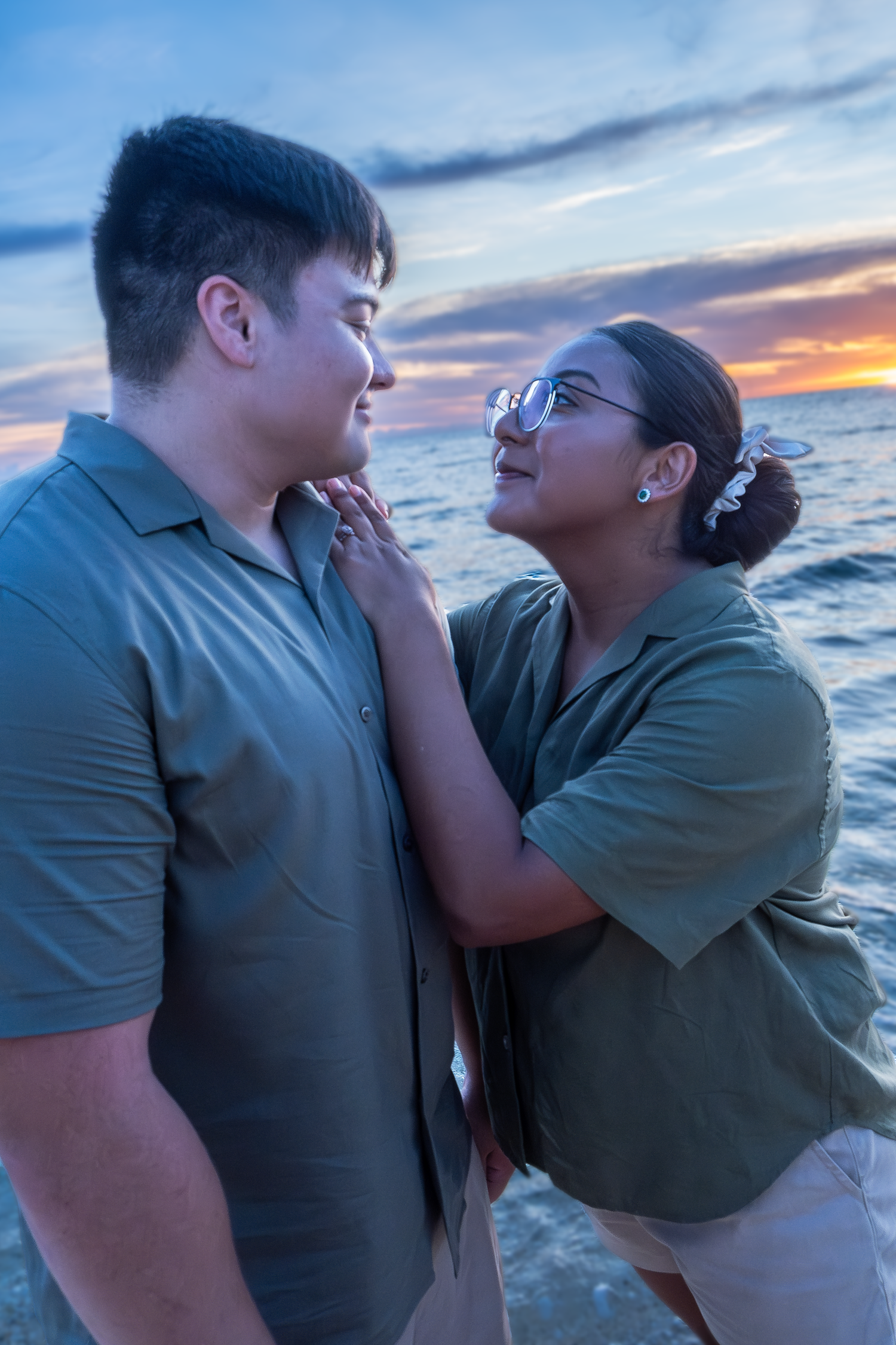 A couple shares an affectionate moment at sunset by the ocean.