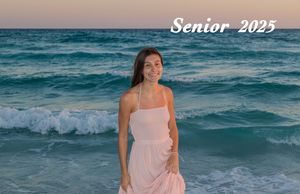 A person in a pink dress poses on the beach at sunset with turquoise waves rolling in the background.
