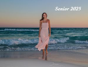 Figure in a flowing pink dress walks along beach at sunset with crashing turquoise waves and soft orange sky.