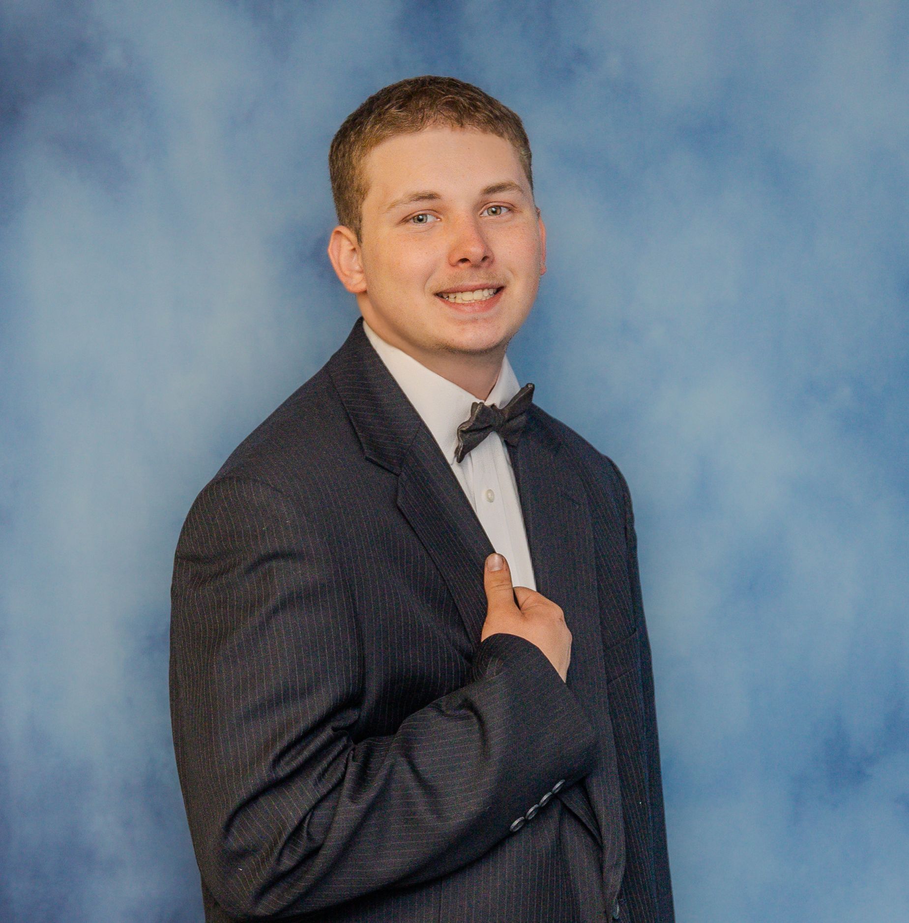 Professional portrait in dark pinstripe suit with bowtie against mottled blue backdrop.