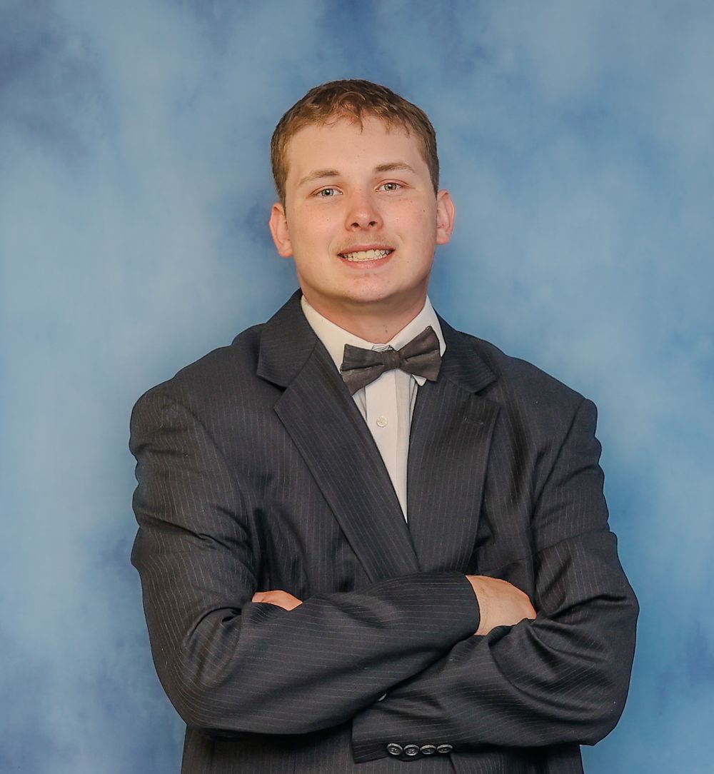 Professional portrait photo of a person in a dark pinstriped suit and bowtie against a blue backdrop.