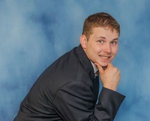 Professional studio portrait with mottled blue background showing a person in a dark suit with hand resting on chin.