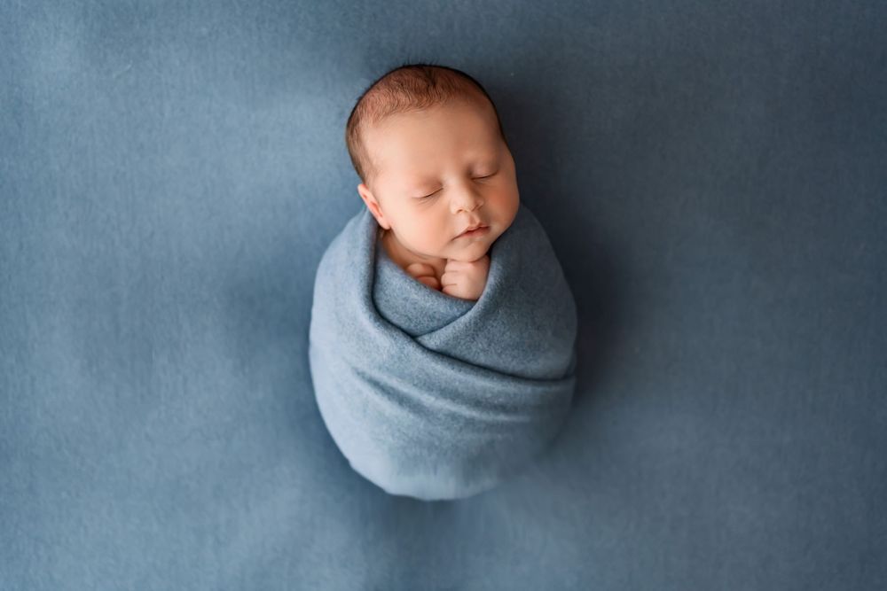 Peaceful sleeping newborn swaddled in soft blue blanket against blue background.