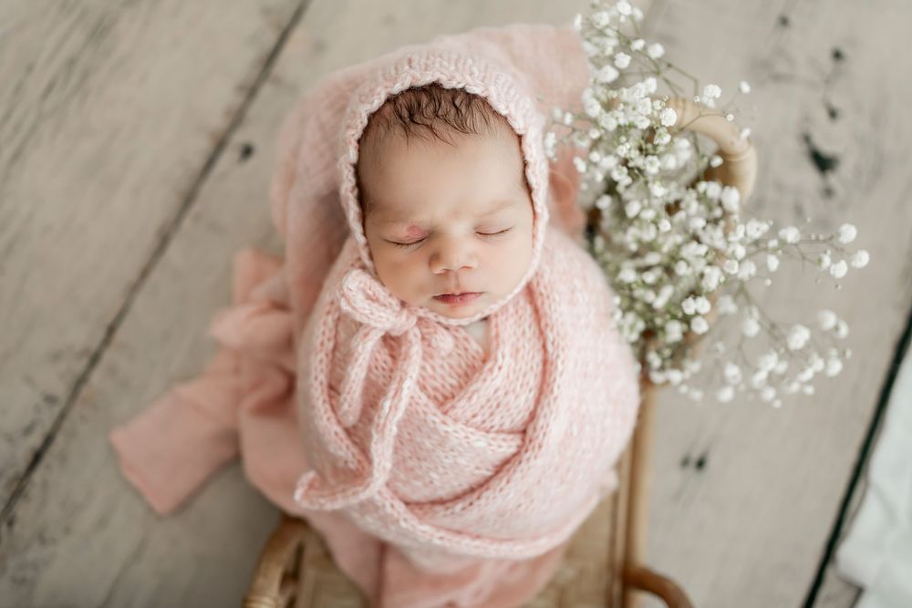Newborn sleeping peacefully on wooden surface with delicate white flowers.