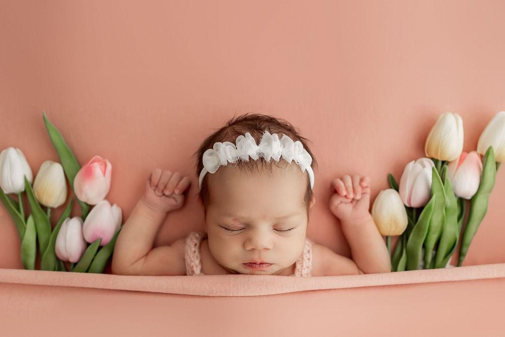Newborn sleeping among pink and white tulips on peach background.