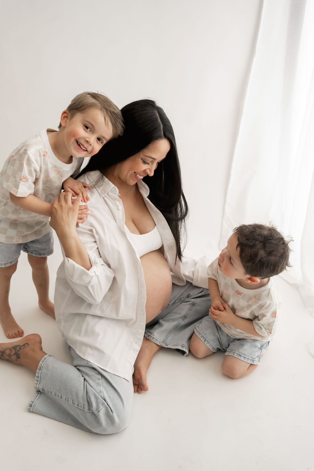 Joyful interaction between pregnant mother and children playing in white studio setting.