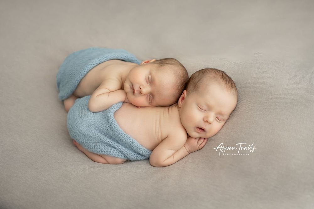 Twin newborns sleeping together wrapped in light blue blankets.