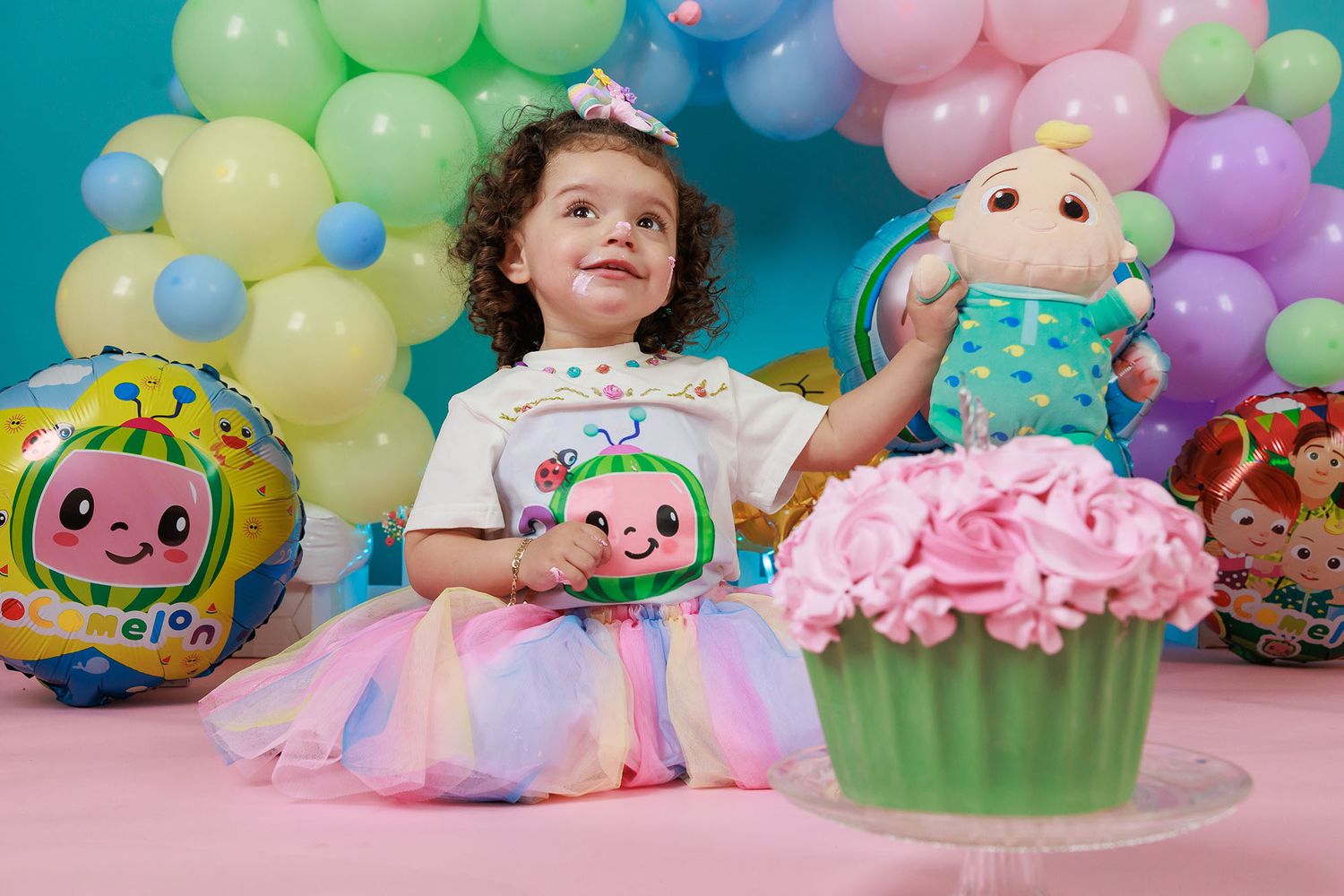 Colorful birthday party setup with a pastel balloon arch, giant cupcake decoration, and Cocomelon themed decorations.