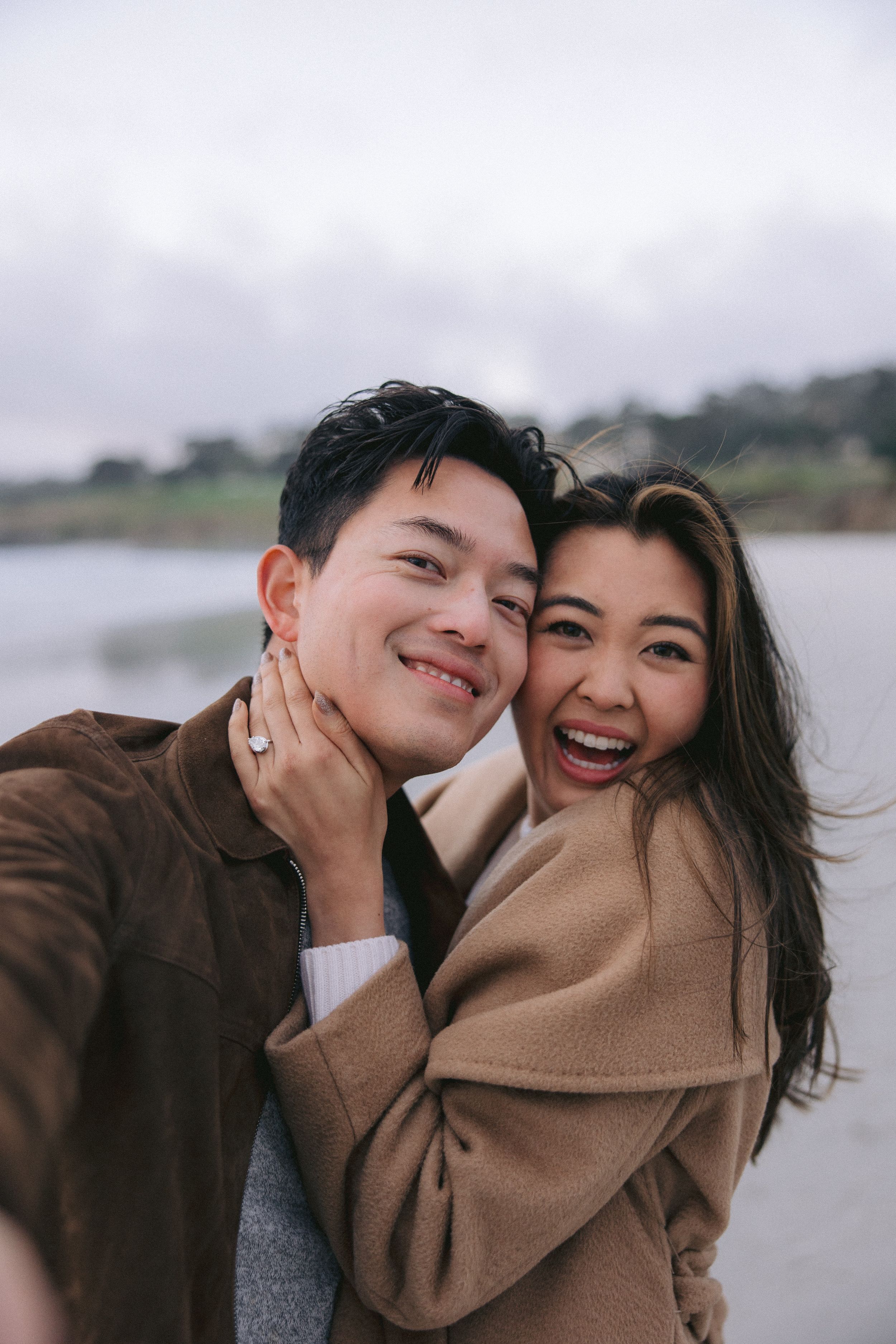 Happy couple in brown coats sharing a joyful moment together outdoors on an overcast day.