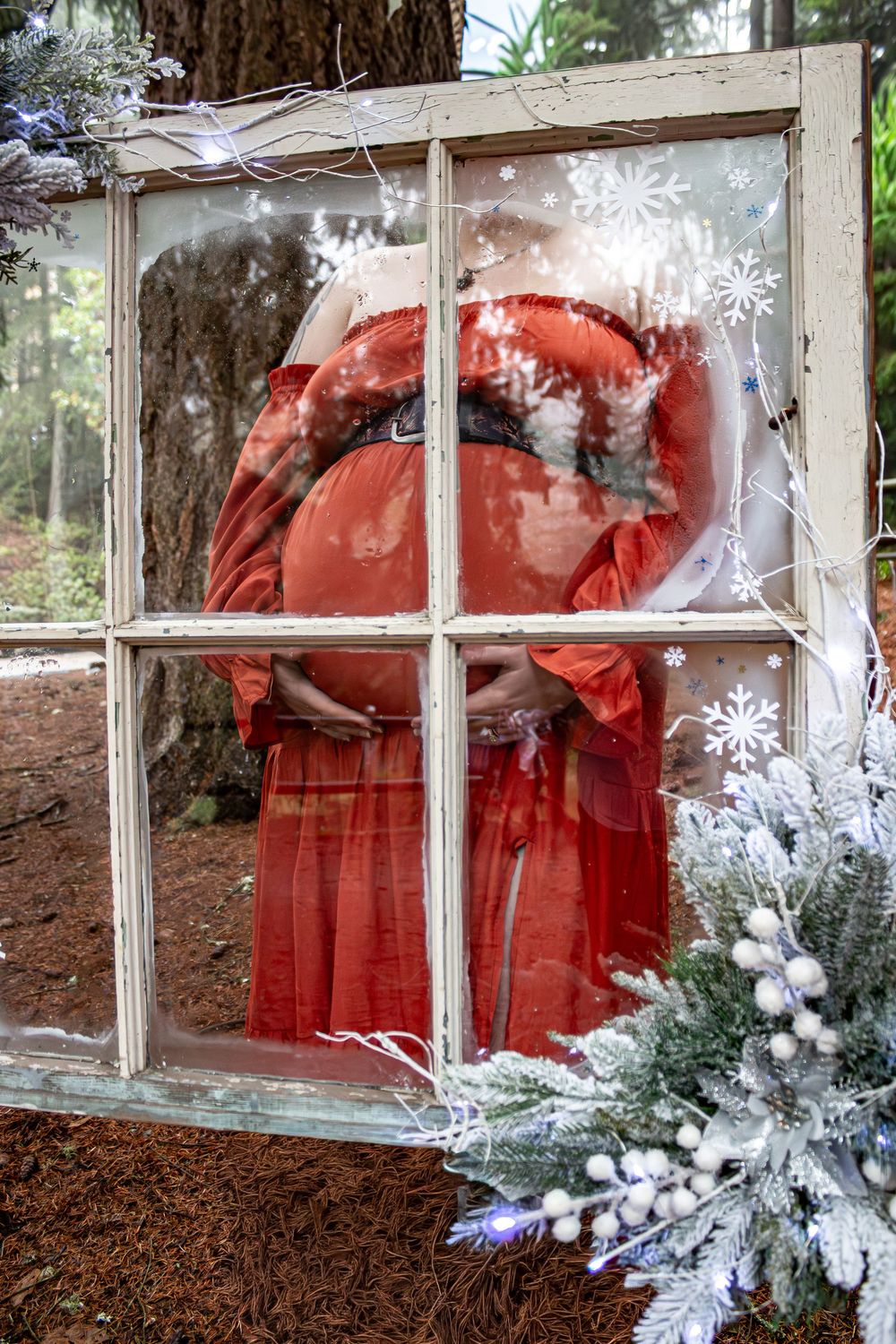 Festive window display featuring red Christmas decorations with frosted pine branches and white snowflakes.
