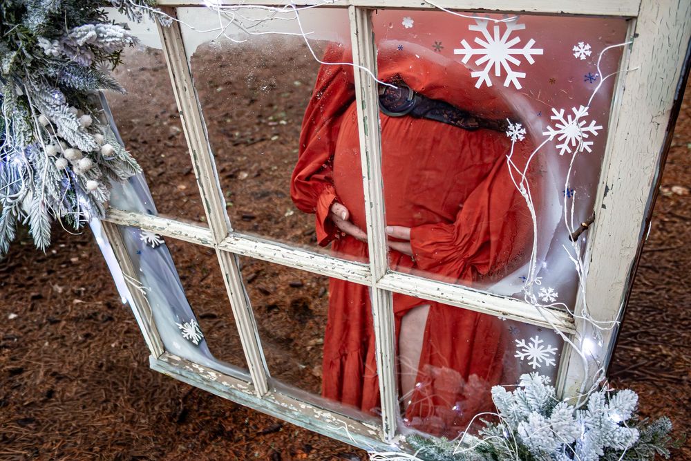 White snowflake ornaments and winter decorations adorn a vintage window frame against a festive red backdrop.