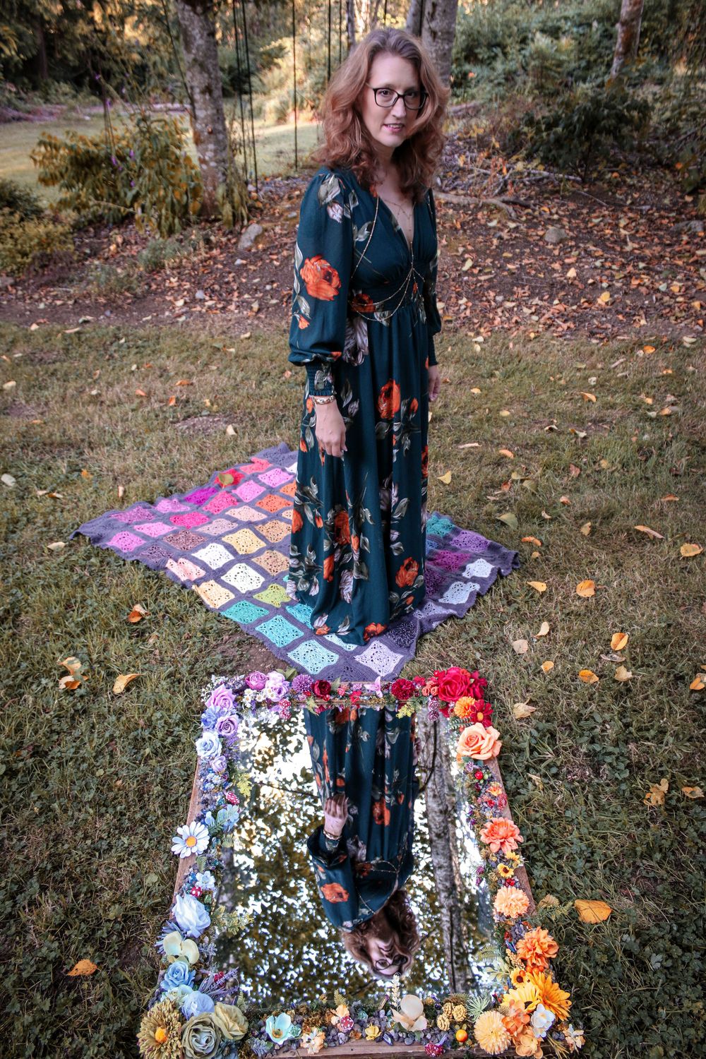 A magical mirror reflection setup in autumn woods with floral decorations and a patterned maxi dress.