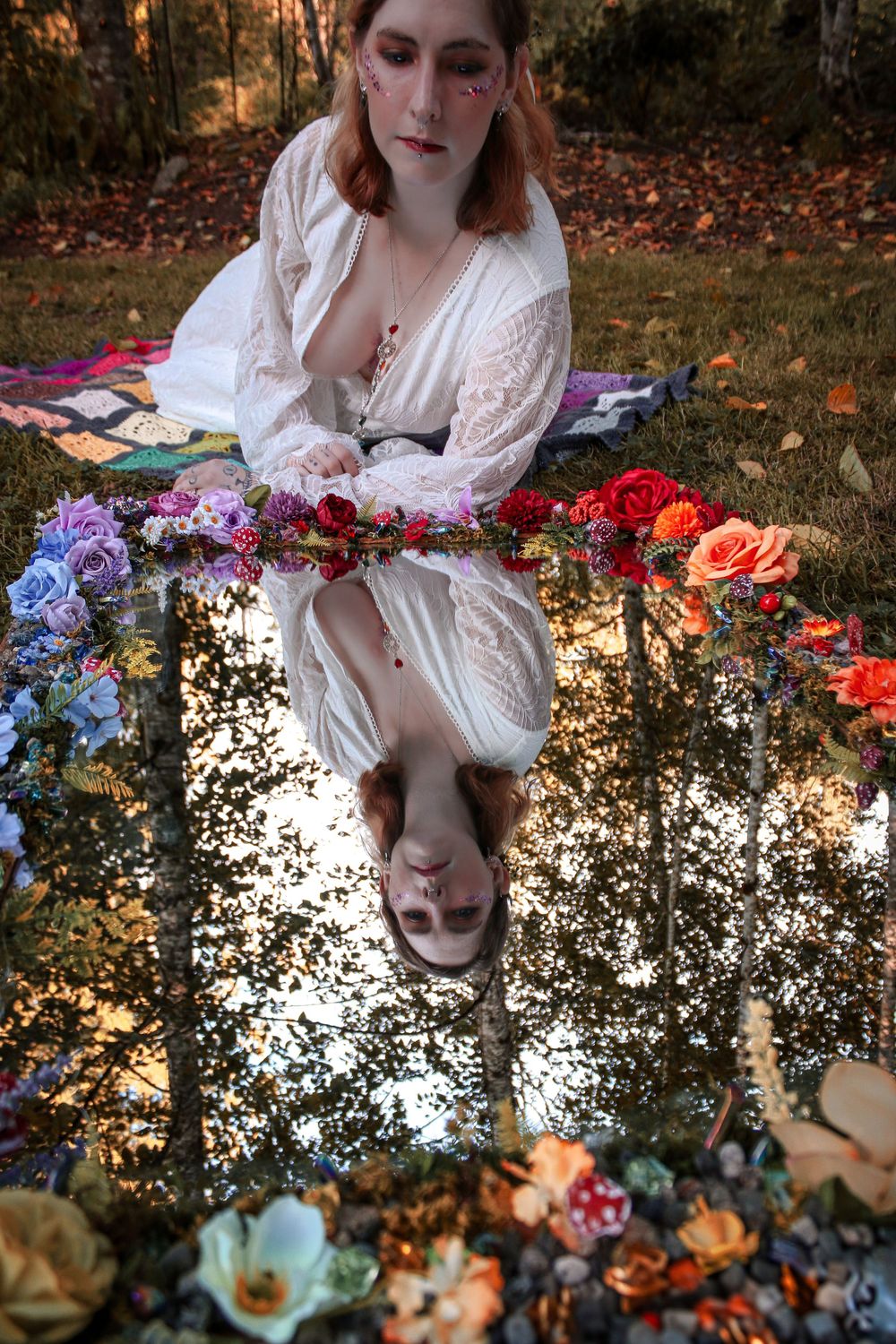 An ethereal scene with white lace dress and vibrant flowers reflected in a mirror-like puddle in autumn.
