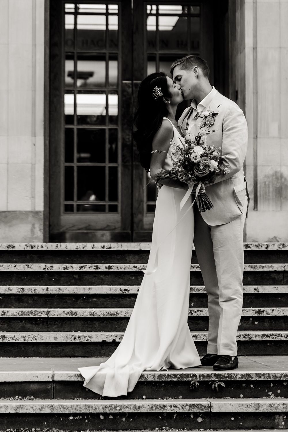 Elegant couple share intimate moment on stone steps of historic building.