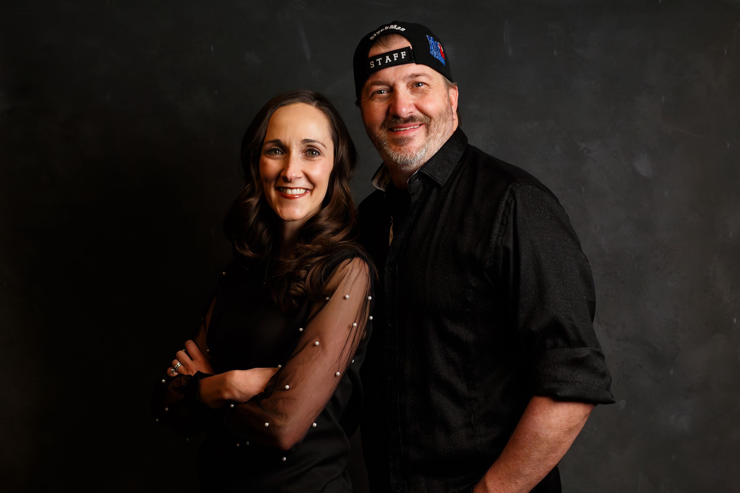 Award winning country radio DJ Mo & Styckman against a dark backdrop, with the woman in a sparkly dress and the man wearing black and a cap.