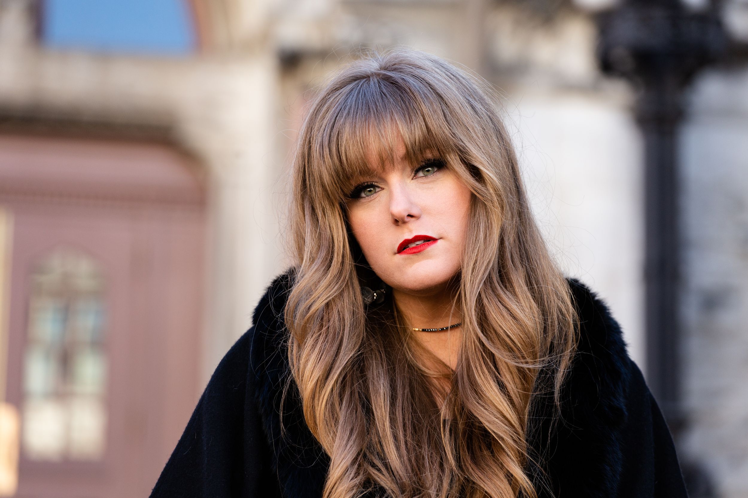 Country artist Deidre Thornell wearing black winter coat outdoors with long wavy brown hair and bangs on a sunny day.