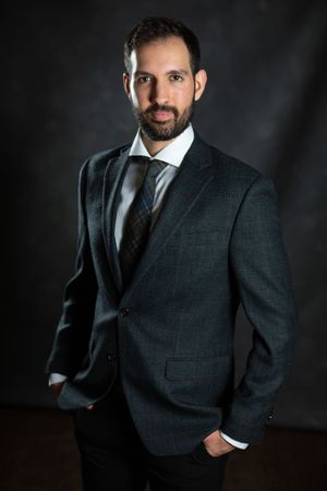 Professional studio portrait of musician Dylan Morris in dark business suit with striped tie against dramatic black background.
