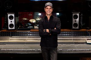 Grammy nominated record producer Sal Oliveri stands with crossed arms in front of a professional audio mixing console in a recording studio.