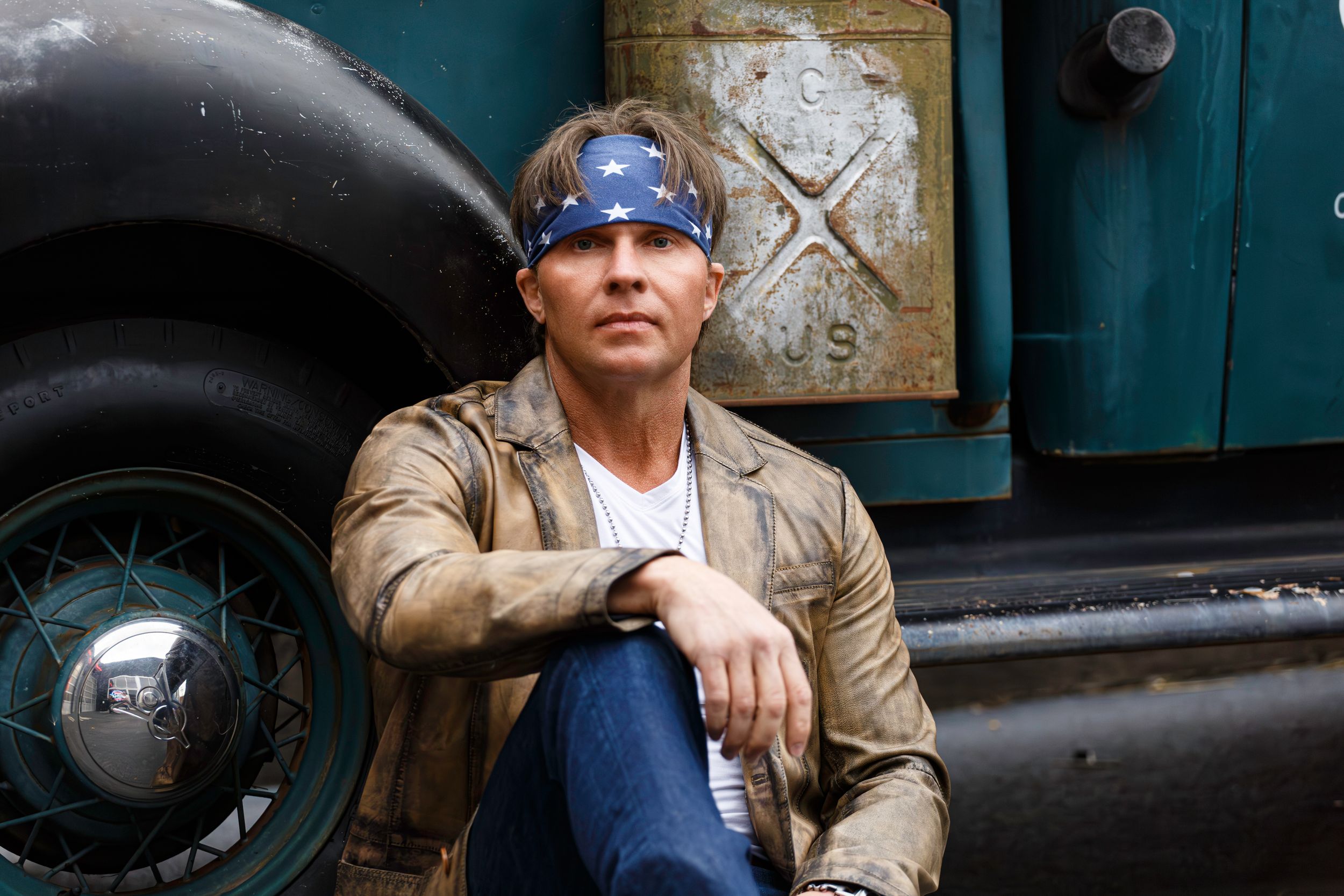 Musician Glen Templeton in a leather jacket and bandana sitting against an industrial backdrop with vintage truck tire and rustic signage.